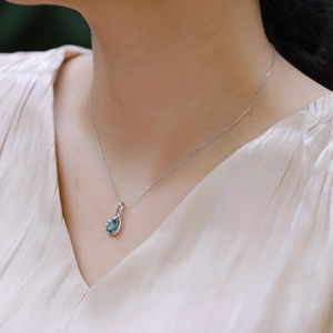Detail of drop-shaped green gemstone pendant necklace on model with beige silk shirt