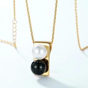 Macro view of gold rectangular pendant with white pearl and black bead on fine cross chain