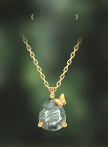 Macro detail of teardrop moss agate pendant with a gold butterfly on a gold chain