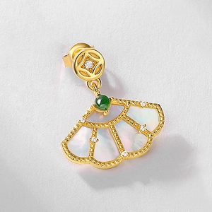 Detailed macro shot of a gold fan-shaped earring with white shell and green emerald