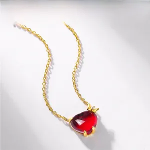 Detail of red heart ruby necklace with gold bow and diamond accent on white background