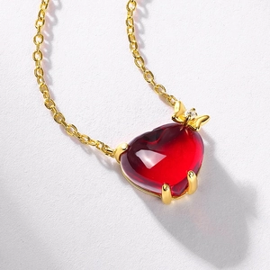 Elegant gold heart pendant necklace with ruby-colored stone and bow detail on grey background