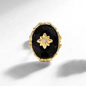 Macro detail of oval black onyx earring featuring a gold star flower and diamond center