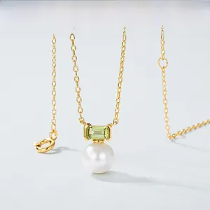 Macro shot of gold necklace with emerald-cut green gemstone and white pearl pendant