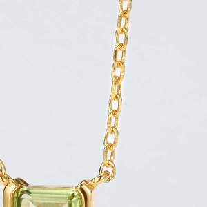 Detail of emerald cut green gemstone pendant on polished gold O-chain necklace