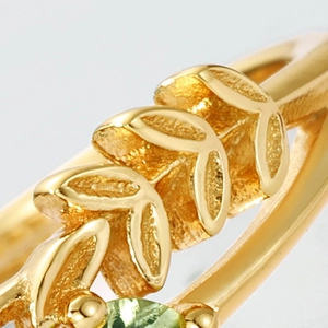 Vue macro d'une bague dorée avec pierre précieuse verte et gravures de feuilles