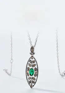 Macro shot of an oval emerald pendant with silver leaf detailing and sparkling accents