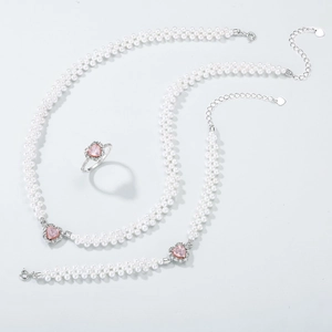 Parure de bijoux élégante avec cristaux cœur roses et perles sur fond gris épuré