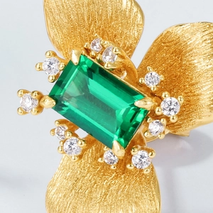 Primer plano de pendientes florales dorados con esmeralda rectangular y diamantes