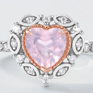 Détail macro d'une bague coeur avec pierre rose, bords en or rose et éclats de zircon