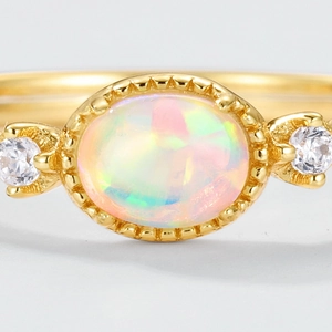 Détail macro d'une bague S925 plaquée or avec opale ovale et zircons latéraux
