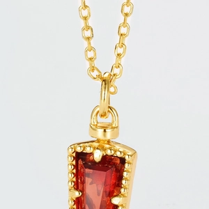 Détail macro du pendentif rubis rouge trapézoïdal avec bordure perlée dorée sur chaîne