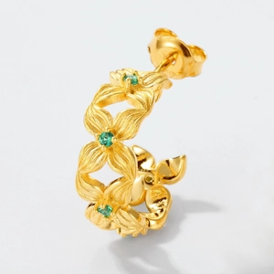 Makroansicht goldener Blumenohrringe mit grünen Schmucksteinen und feiner Blütenstruktur