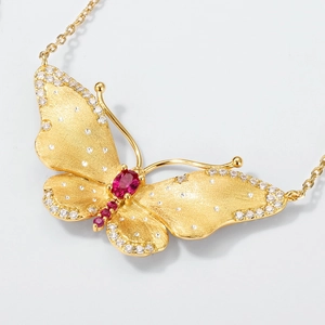 Macro detail van de gouden vlinder hanger met matte finish en rode edelstenen
