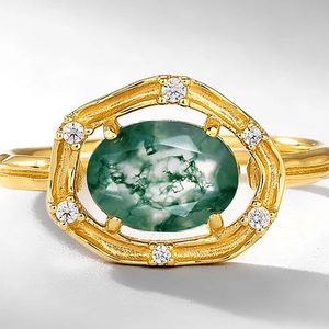 Macro detail of oval moss agate ring in gold frame with textured finish and zircon accents