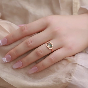 Close-up of moss agate ring on hand over silk, featuring a rose gold halo setting