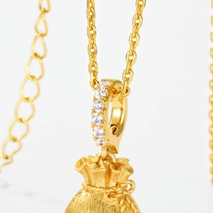 Macro detail of gold lucky bag pendant with brushed texture and sparkling zircon inlay