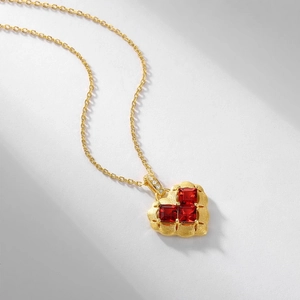 Matte gold heart necklace with red stones and brushed finish on white surface