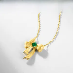 Detail of gold bow necklace with brushed texture, emerald stone and pavé zircons