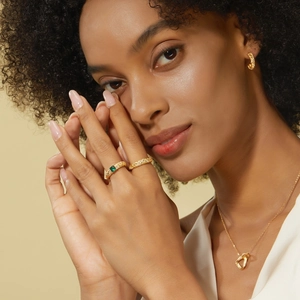 Close-up of a model wearing gold woven texture rings with a green gemstone and jewelry set