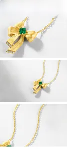 Macro shot of gold bow necklace with emerald gemstone and brushed metal texture details