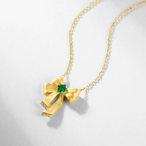 Bow necklace in brushed gold finish with emerald stone and diamond accents