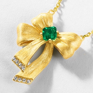 Detail of gold bow necklace with square emerald and diamond accents on ribbon end