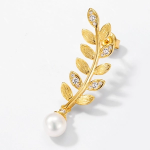 Close-up of leaf-shaped gold earring featuring inset zircon stones and a hanging pearl