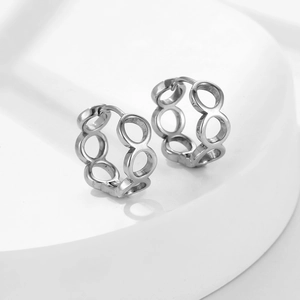 Boucles d'oreilles créoles géométriques ajourées en acier titane sur socle blanc
