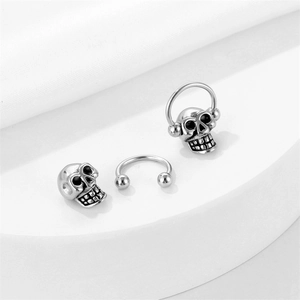 Gothic punk style stainless steel skull studs with horseshoe ring on a white platform