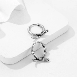 Retro stainless steel snake hoop earrings with detailed scales on white stone surface