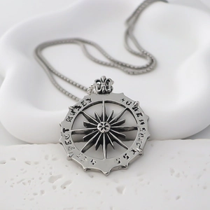 Detailed macro of vintage silver compass pendant with gothic lettering on a pearl chain