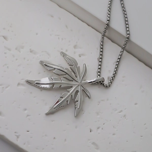 Macro d'un pendentif feuille d'érable argenté sur une chaîne sur socle blanc
