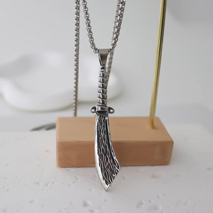 Macro detail of silver dagger pendant with textured relief on a stainless steel box chain
