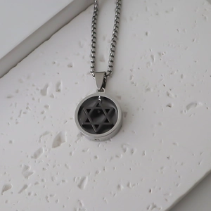 Gros plan d'un pendentif hexagramme argenté sur chaîne box sur texture pierre blanche