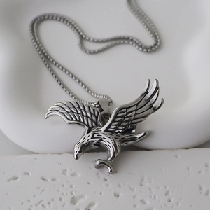 Détail du collier pendentif aigle argenté posé sur un support en pierre blanche