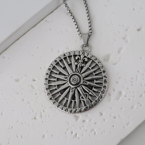 Macro shot of silver compass pendant featuring fleur-de-lis and box chain on white stone