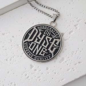 Close-up of a circular DYSE ONE pendant with black drip oil and silver square chain link