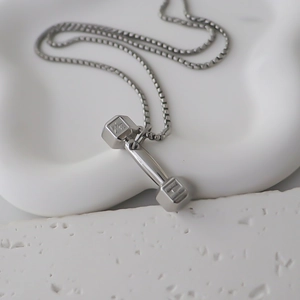 Détail macro du pendentif haltère argenté avec chaîne carrée sur surface texturée