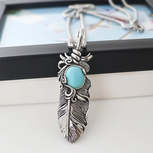 Vintage silver feather pendant necklace with oval turquoise stone on black background