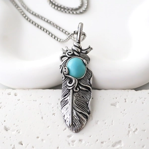 Close-up of vintage silver feather pendant with turquoise stone inlay on white stone base