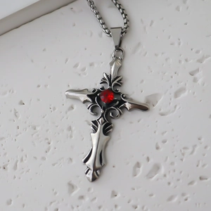 Macro shot of silver gothic cross pendant with red gemstone on textured stone surface