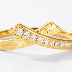 Close-up of golden ribbon ring featuring brushed texture and micro-pave zircon setting
