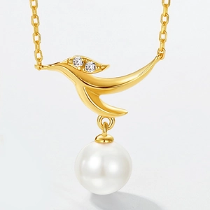 Macro detail of bird-shaped gold necklace pendant with zircons and a large round pearl
