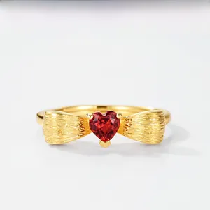 Detail of gold bow ring with a red heart gemstone and brushed metal finish