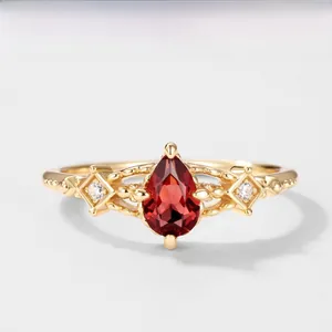 Macro di anello dorato con granato a pera e dettagli in diamante sui lati
