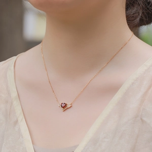 Elegant gold necklace with red heart gemstone and V-shaped diamond accents on model