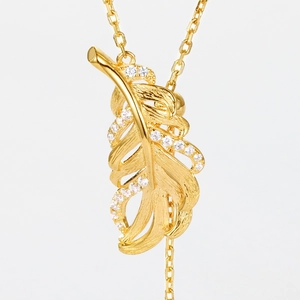 Detail of leaf pendant necklace with gold finish and white crystals on brushed silver