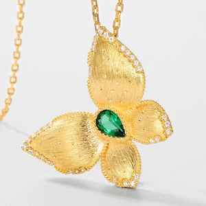 Détail macro du pendentif papillon doré avec finition brossée et pierre verte sertie