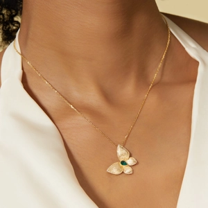 Collier papillon doré avec texture brossée et pierre verte porté par un mannequin